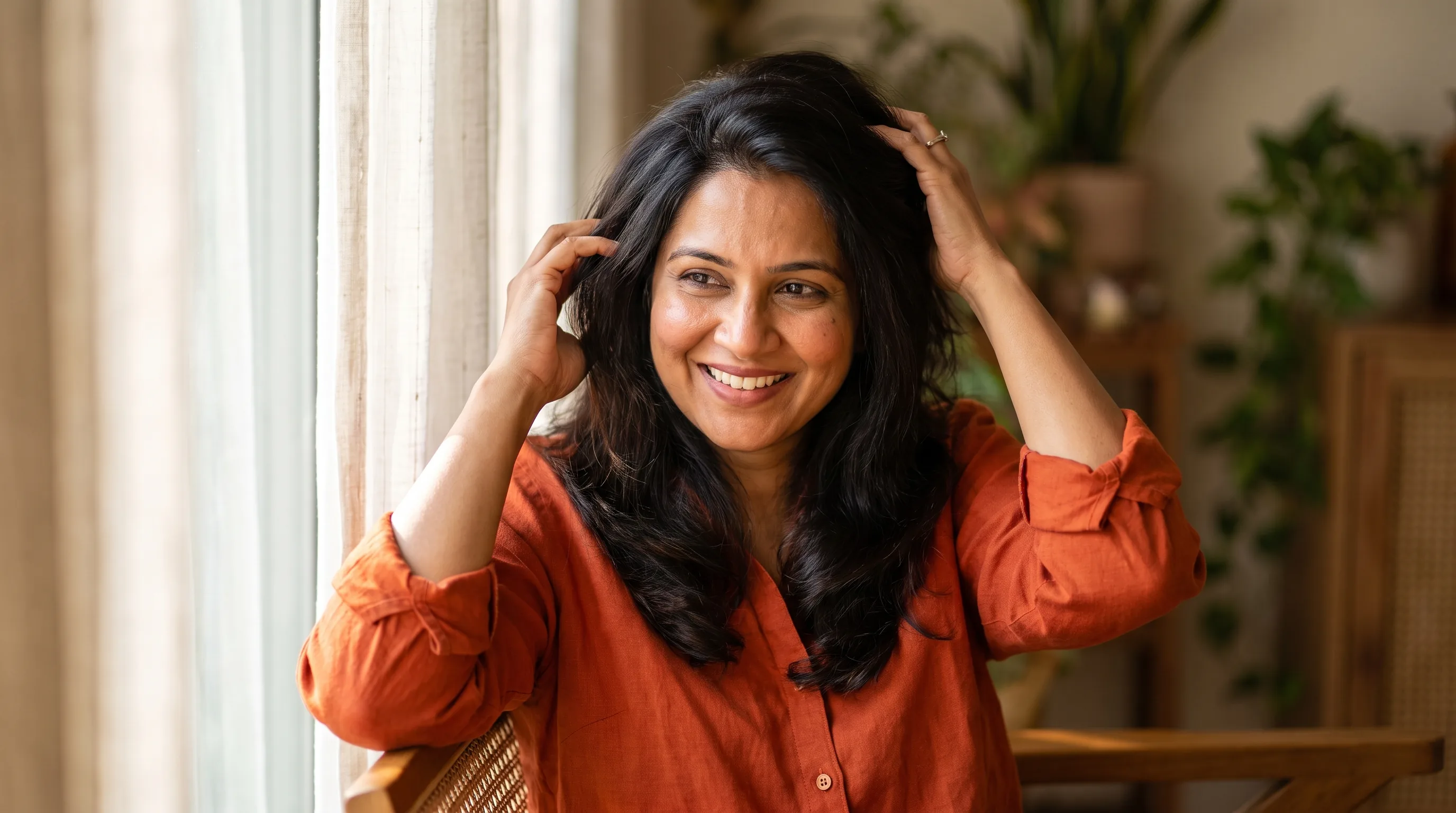 A woman in her forties running her fingers through healthy, shiny hair in soft natural morning light