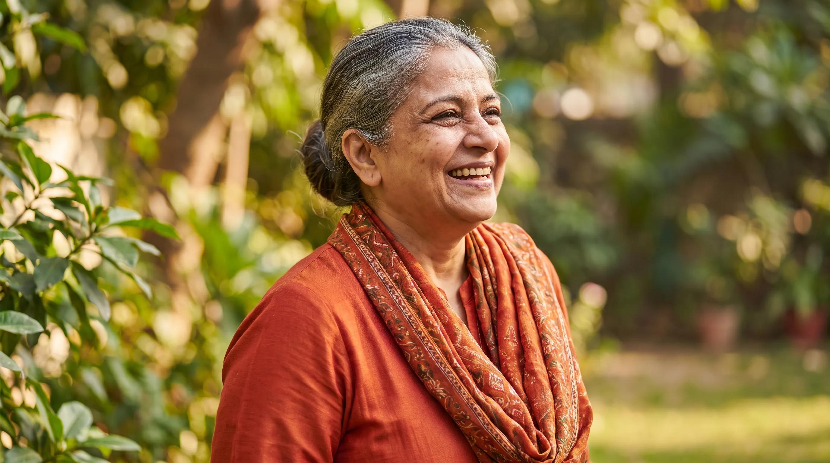 A woman in her late 30s with clear, radiant, even-toned skin laughing in soft natural daylight outdoors