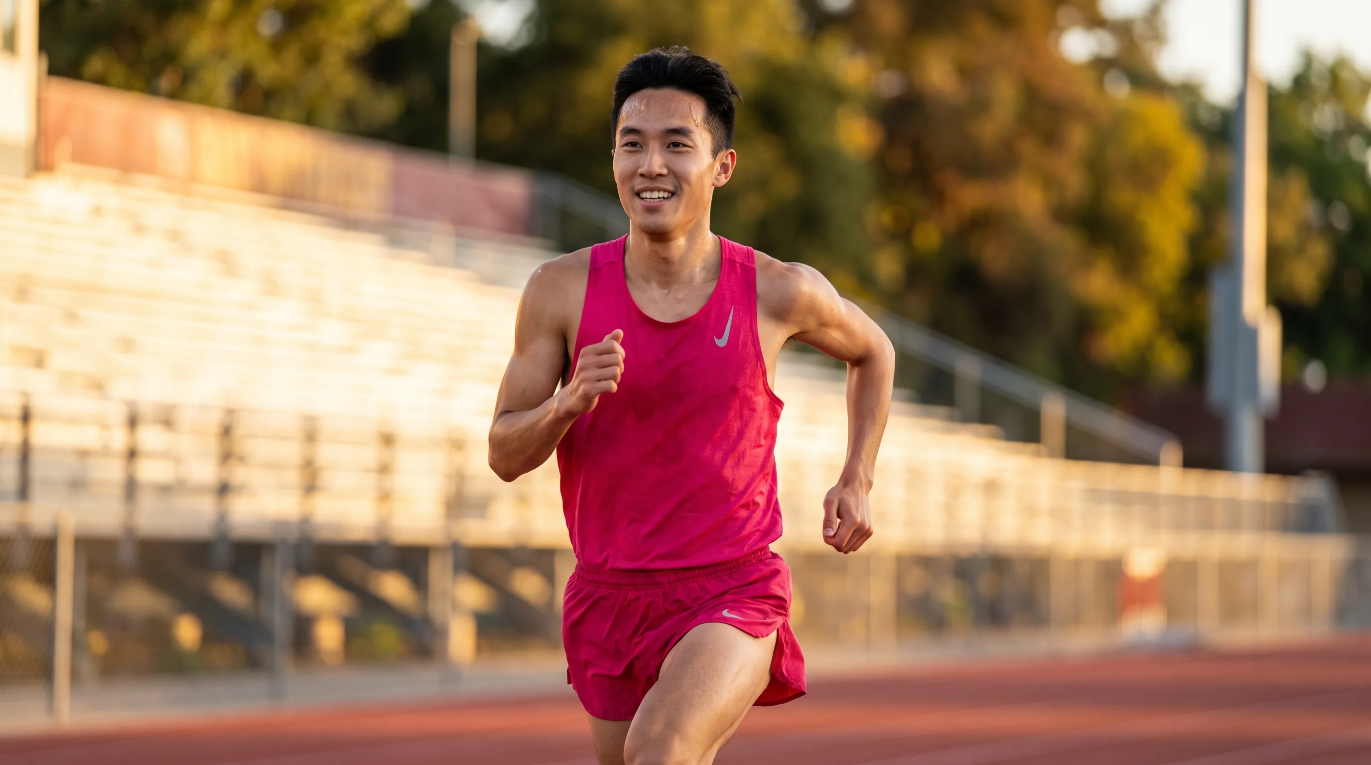 A lean, athletic man in their 20s sprinting on a track at sunrise