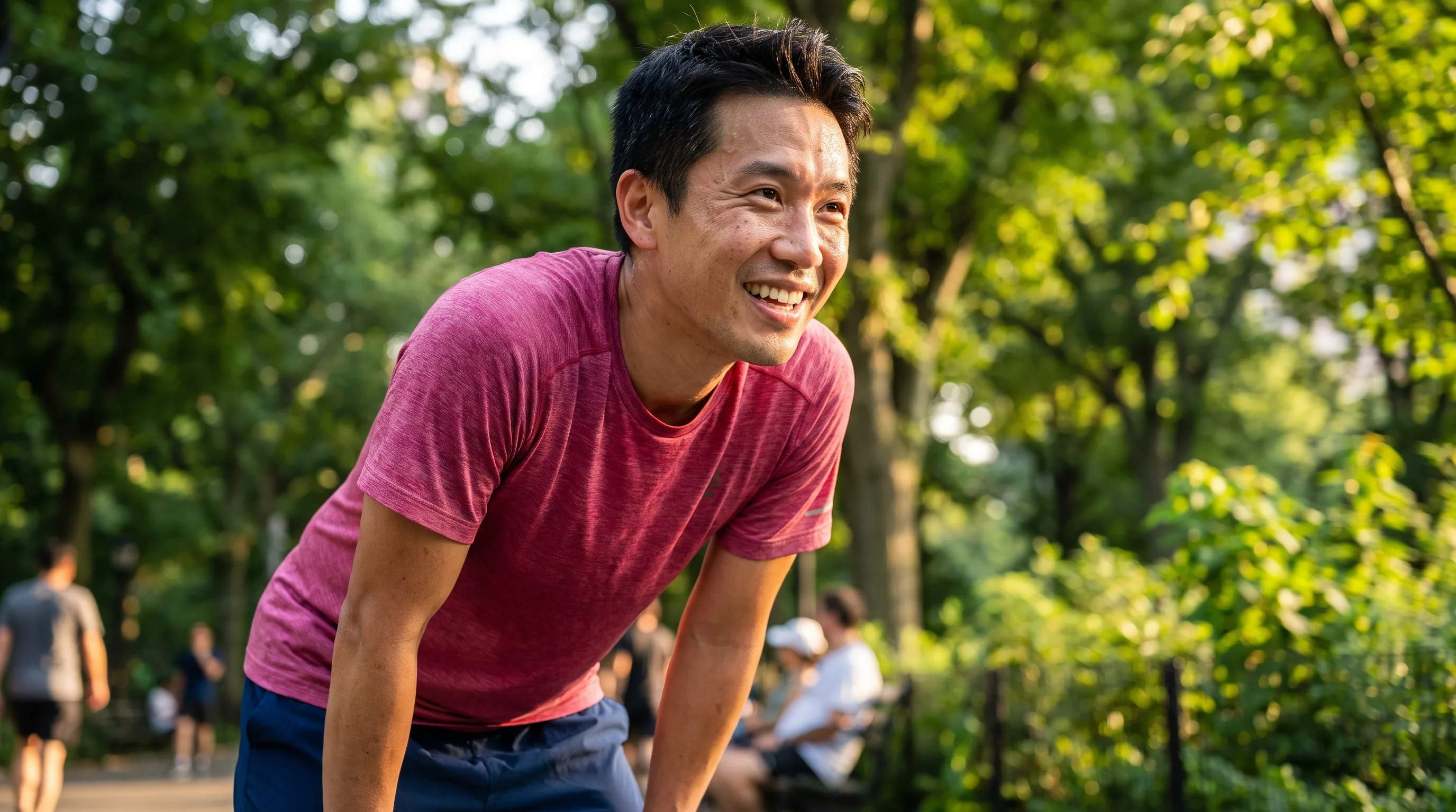 A warm, happy photo of a healthy man in his early forties smiling in bright morning sunlight after a run in the park, relaxed and full of energy.