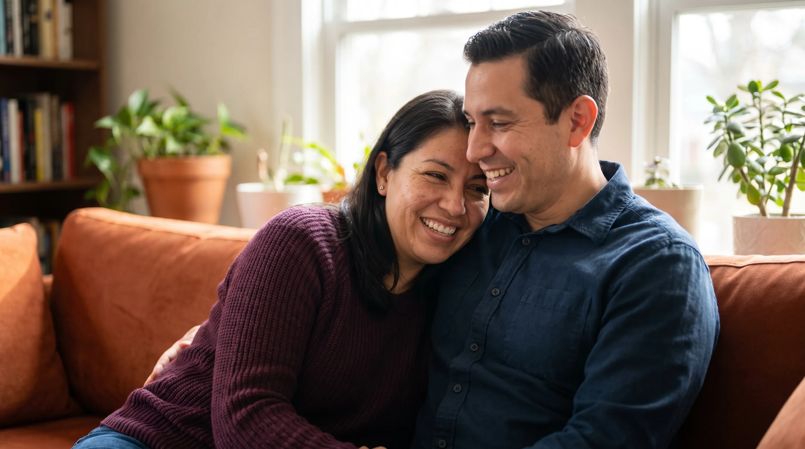 A confident, healthy couple in their late thirties sharing a warm, relaxed moment together at home, close and affectionate, softly lit, fully clothed and non-explicit